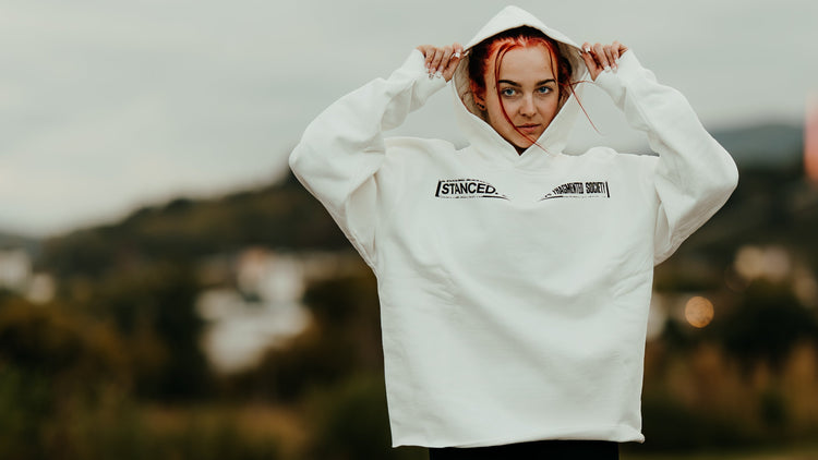 Person wearing a white hoodie with text, standing on a road with a blurred background