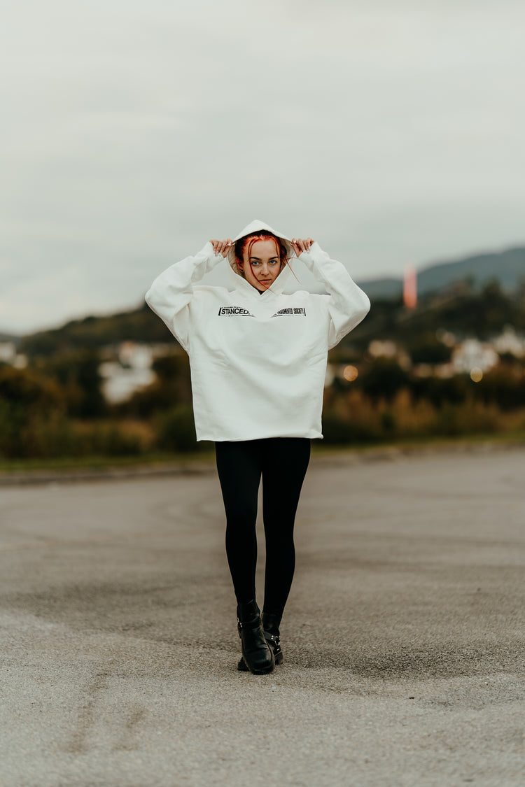 Person wearing a white hoodie with text, standing on a road with a blurred background